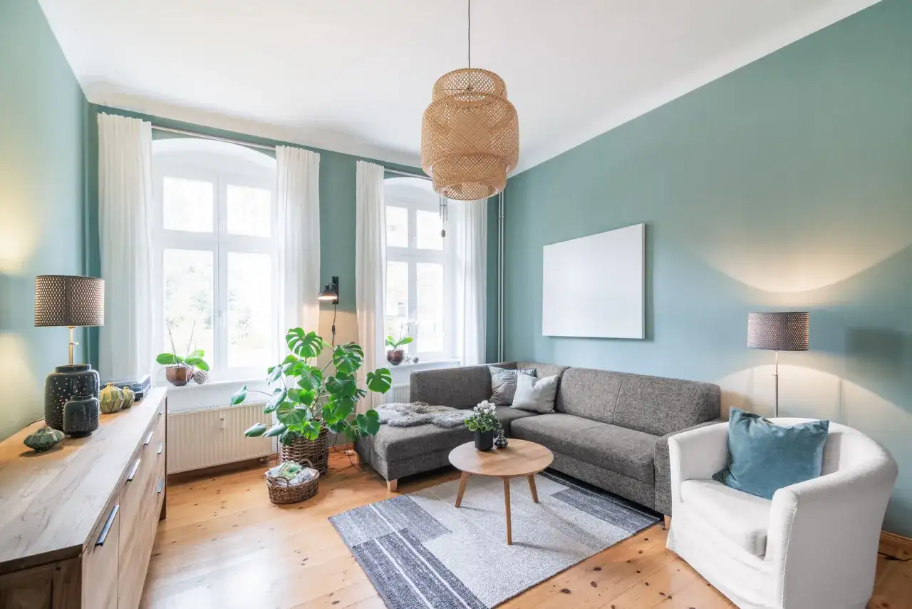 Wohnzimmer mit Sofa, Sessel, Holztisch und Pflanzen. Die Wandfarbe und die natürlichen Materialien schaffen eine harmonische Feng Shui Atmosphäre.